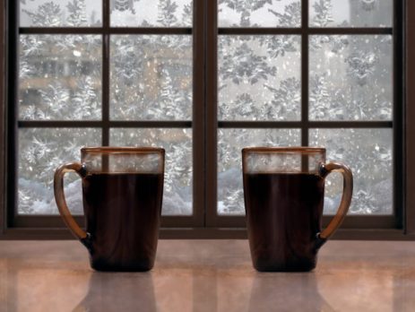 2 cups of coffee in from of a window with snow covered trees outside